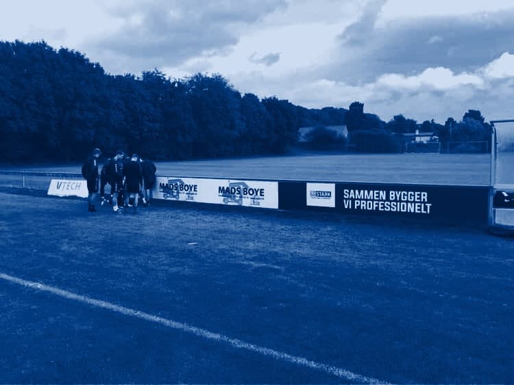 Spillere samlet ved sponsorbanderne langs en fodboldbane